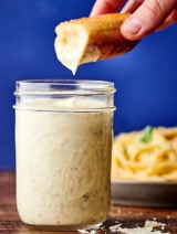 breadstick being dipped in jar of alfredo sauce