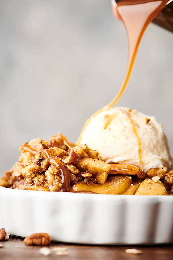 Dish of apple crisp with vanilla ice cream and caramel sauce being drizzled on top side view