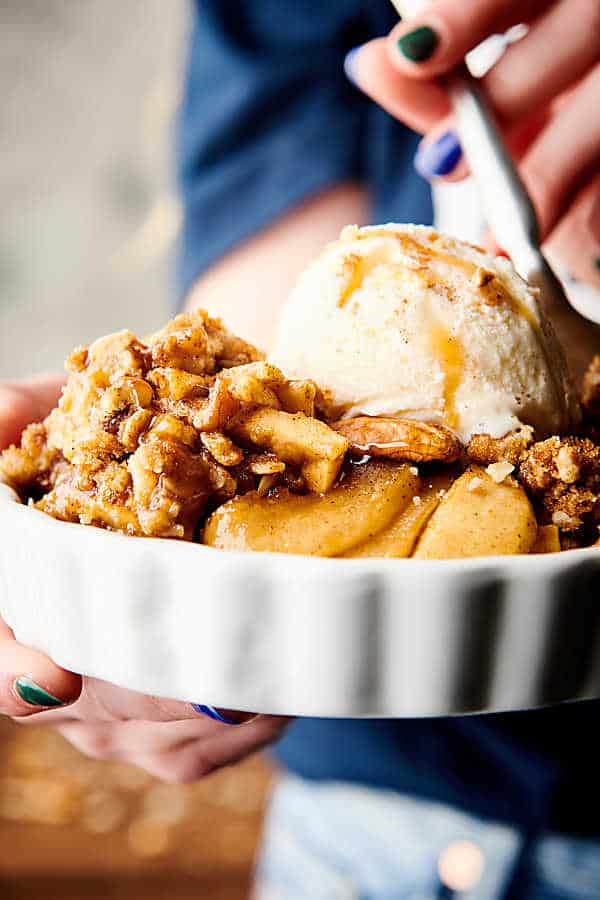 Dish of apple crisp with ice cream and caramel drizzle held with fork