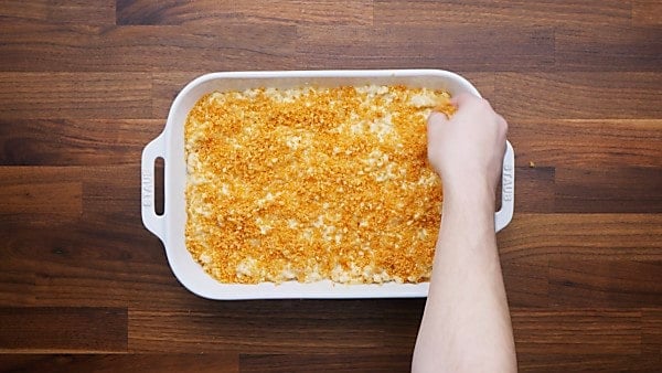 Topping being spread over baked mac and cheese