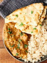 Chicken curry on a plate with naan and rice above