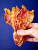 slices of bacon held blue background