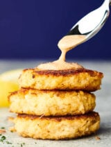 three crab cakes stacked being drizzled with sauce