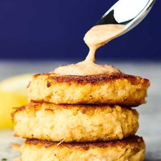 three crab cakes stacked being drizzled with sauce