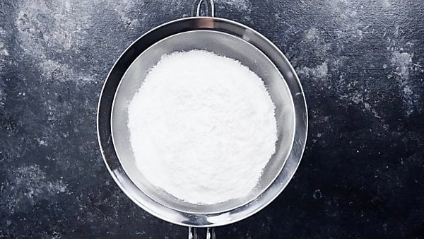 Powdered sugar being sifted through sieve