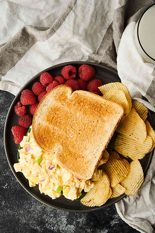 egg salad sandwich on plate with chips and raspberries above