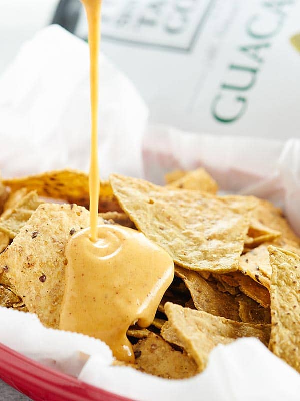 queso being drizzled over basket of tortilla chips