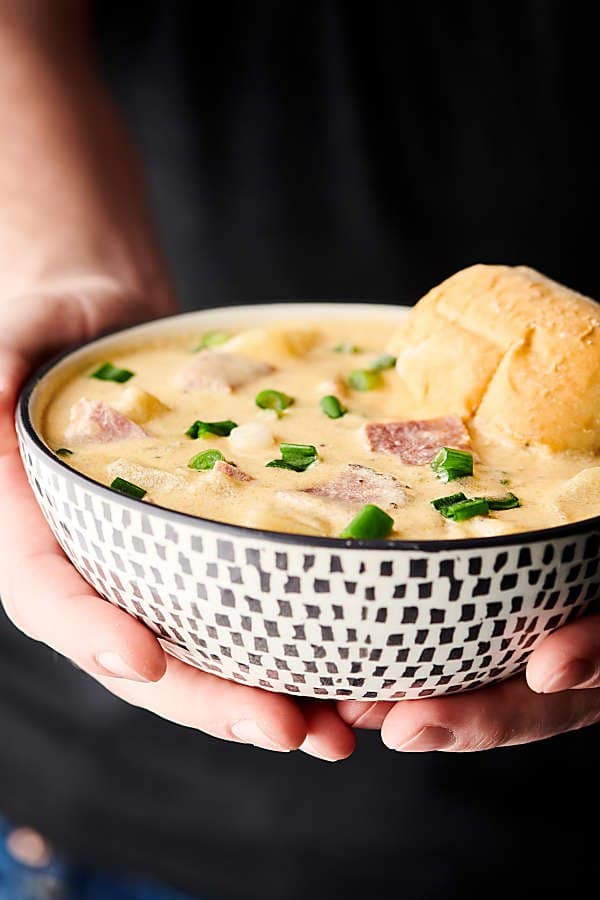 Ham and cheese potato soup in bowl held with two hands 
