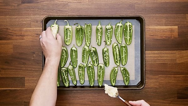 Jalapeno halves being filled with cream cheese mixture and placed on baking sheet