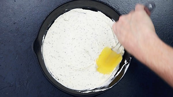 Cream cheese base being spread with spatula into cast-iron skillet