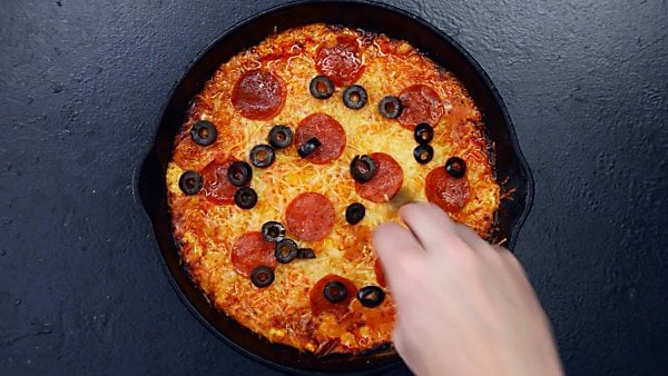 Black olives being layered on baked, loaded pizza dip