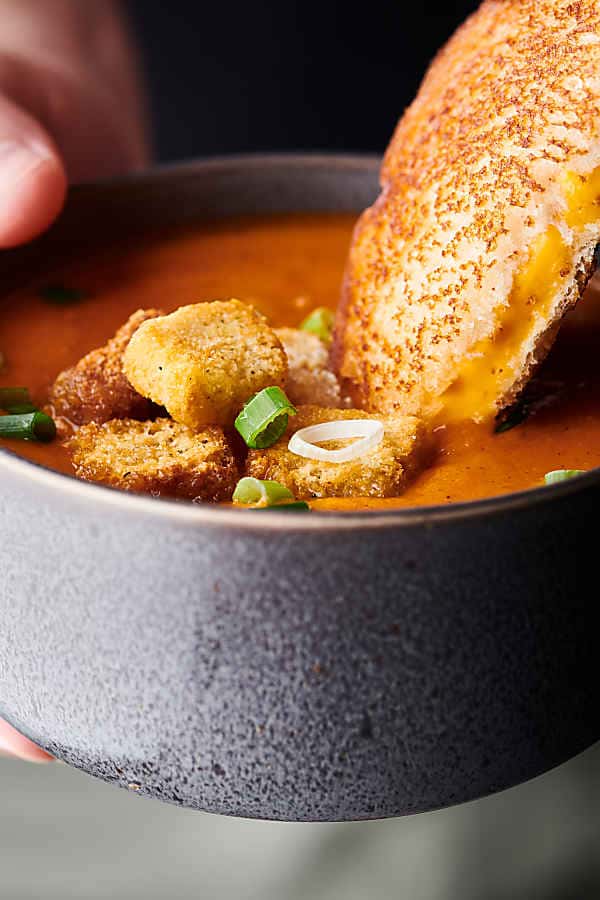 Grilled cheese sandwich being dipped into bowl of roasted tomato soup