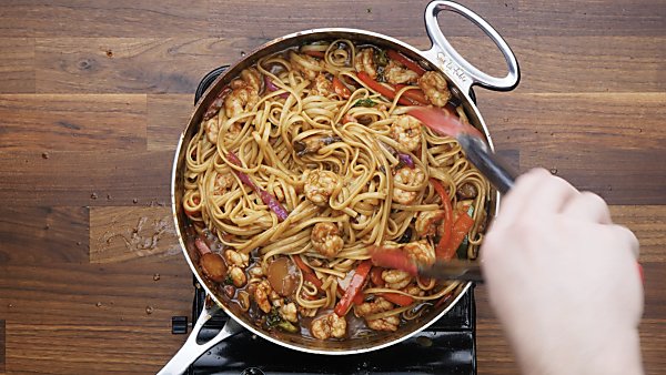 shrimp lo mein in saute pan being served with tongs