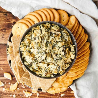 plate of crackers with bowl of spinach artichoke dip