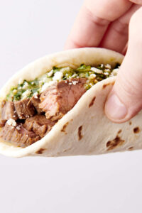 holding a taco with steak and chimichurri