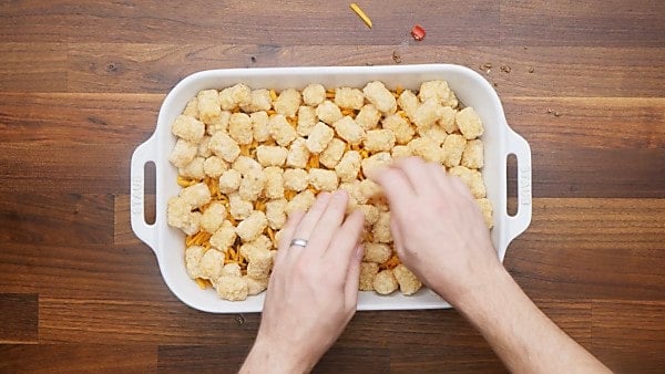 tater tots being layered in casserole dish