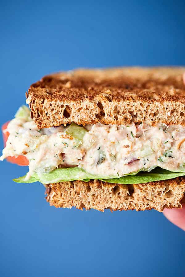 Half tuna salad sandwich held blue background